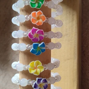 lot de bracelet Tiaré Cristal en perle blanche avec chacun une fleur de tiaré de différente couleur sur un support en bois