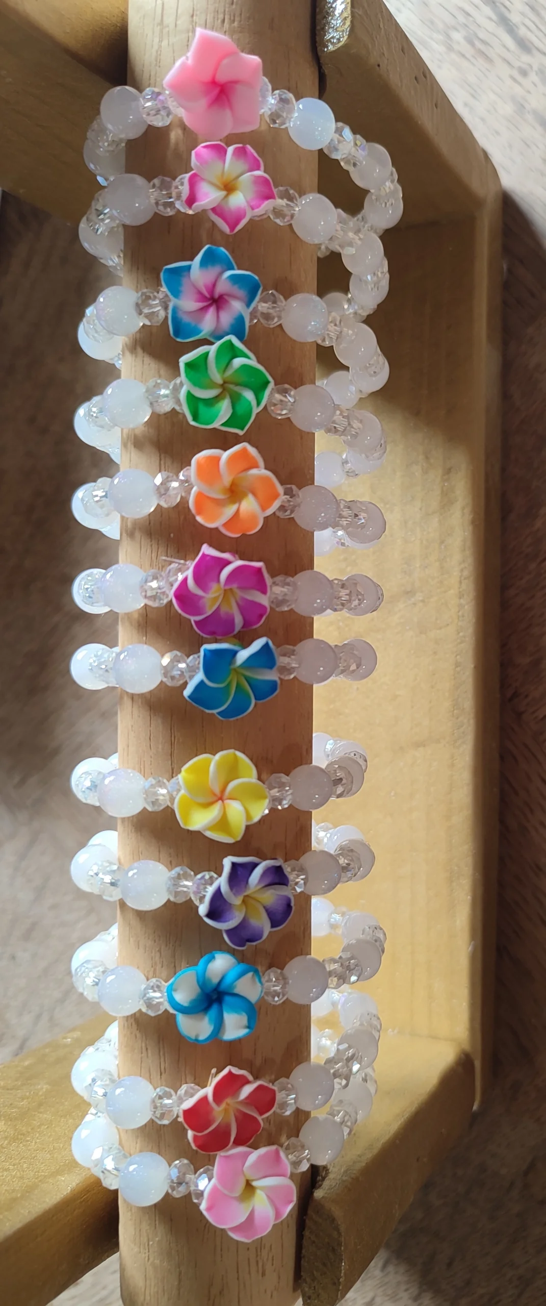lot de bracelet Tiaré Cristal en perle blanche avec chacun une fleur de tiaré de différente couleur sur un support en bois