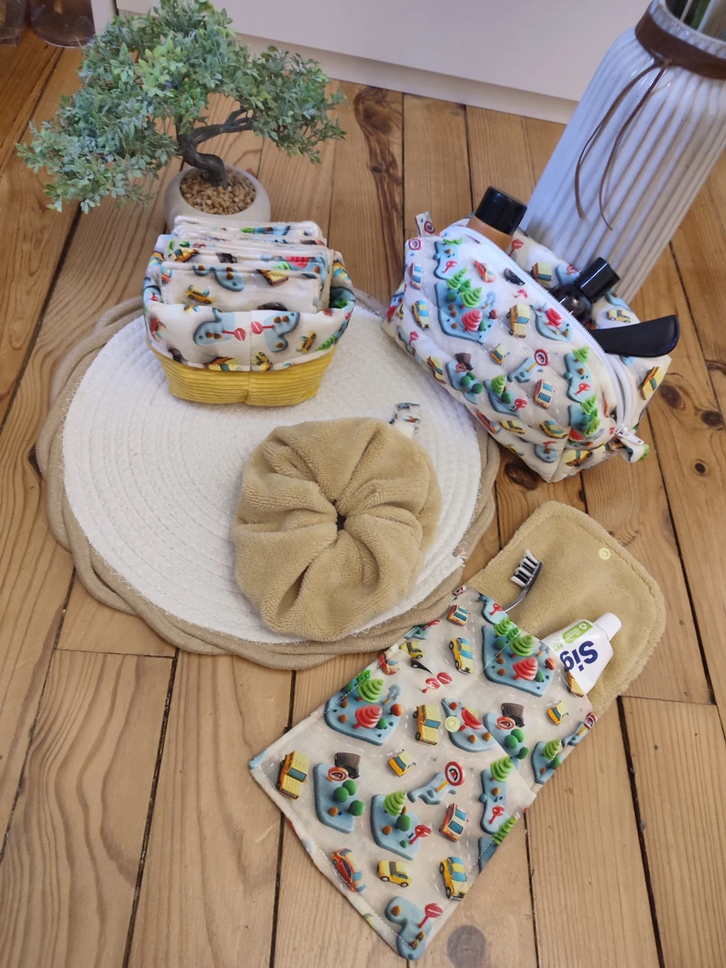 ensemble de la collection Mini Drive comprenant un panier avec des lingettes réutilisables, une trousse de toilette, un essui main et une pochette de rangement brosse à dent de couleur beige avec des motif de de voiture et de route