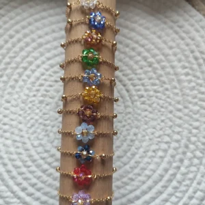 lot de bracelets de couleur or avec au centre un fleur de différentes couleur fait en perle sur un support en bois