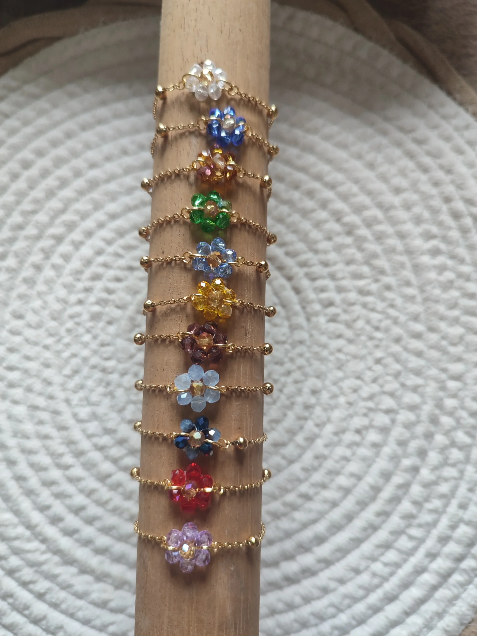 lot de bracelets de couleur or avec au centre un fleur de différentes couleur fait en perle sur un support en bois