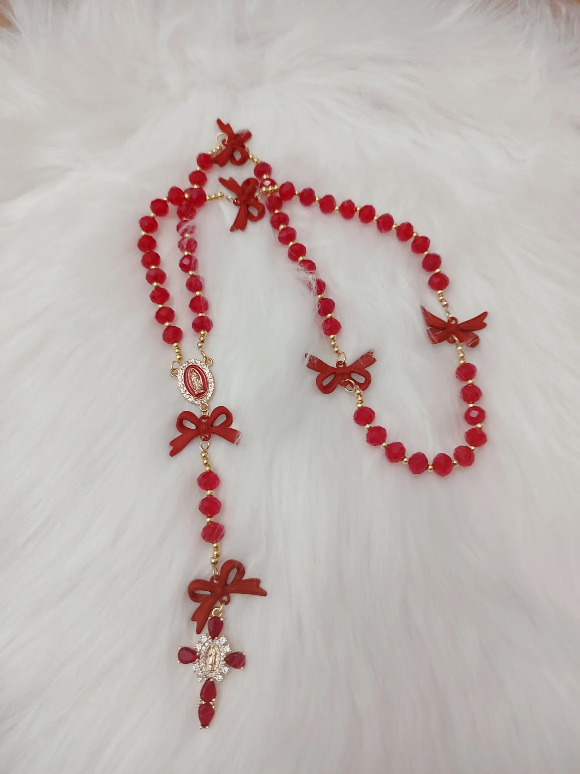 collier Chapelet "Ruban Précieux" avec des perles couleurs rouge, des noeuds rouge et une croix rouge sur un tapis blanc