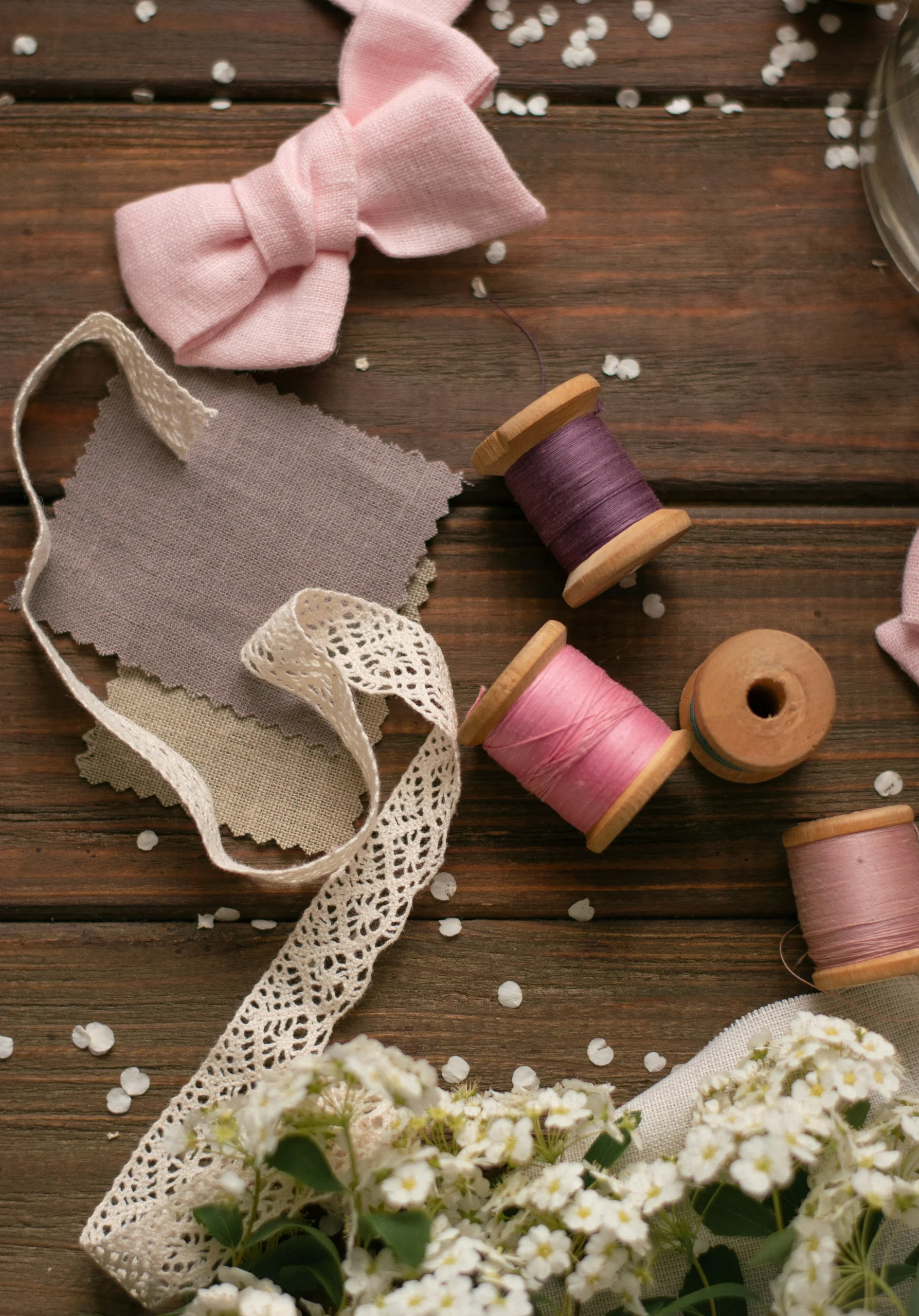 image d'un noeud rose, de bout de tissus beige et taupe et de bobine de fils rose et violet