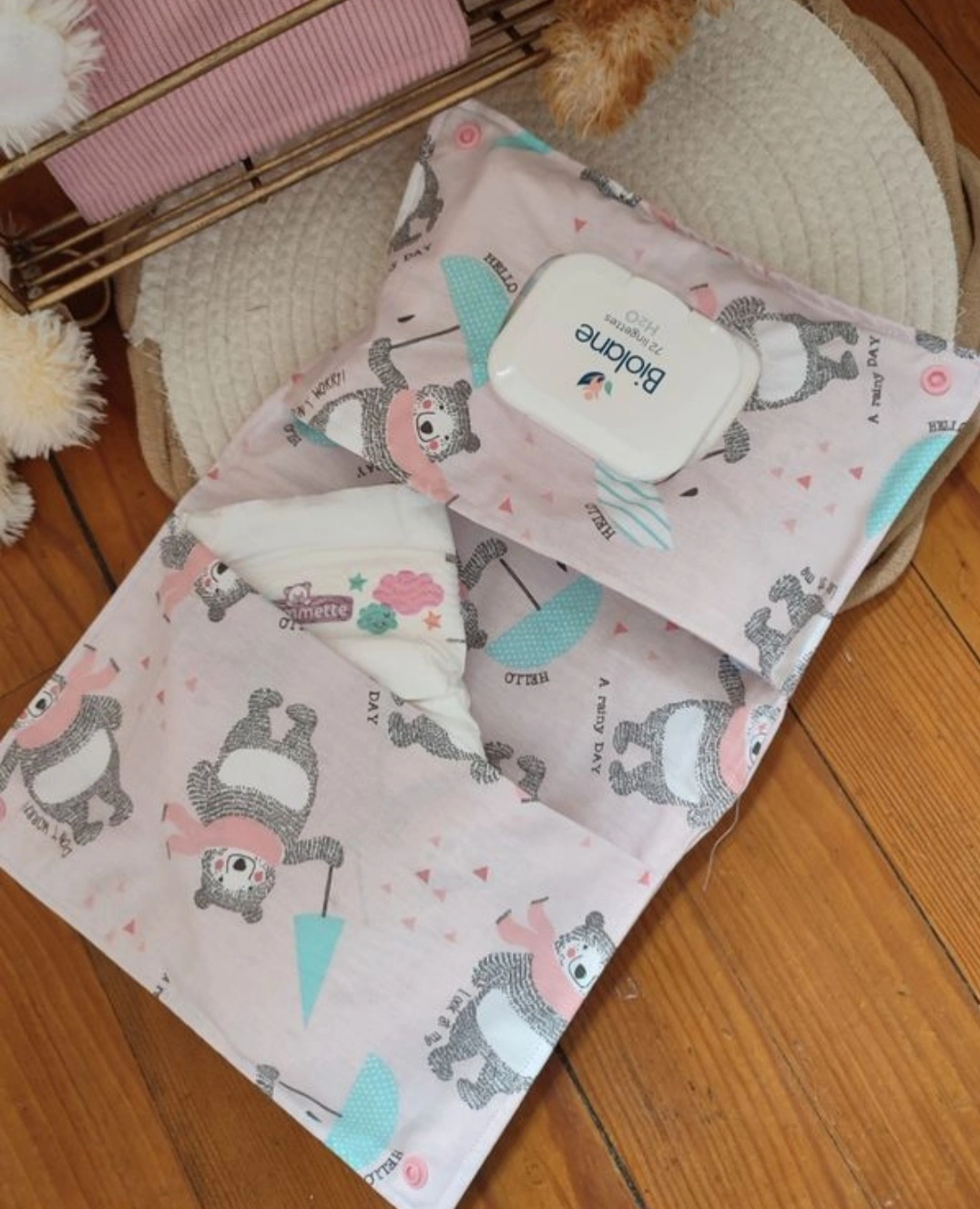 pochette à lange artisanale ouverte, elle est de couleur rose claire avec des motifs d'ours avec un parapluie bleu et une écharpe rose