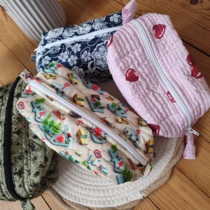 Plusieurs trousse de toilette des collections City Drive, Bandana, Coeur vues du dessus sur un tapis beige