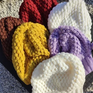 bonnet retombant fait main en crochet de différentes couleurs à la plat sur une table extérieur