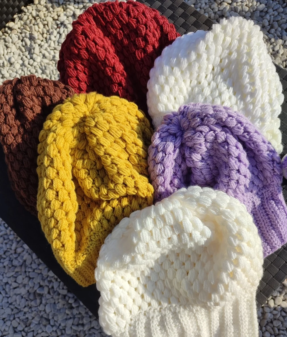 bonnet retombant fait main en crochet de différentes couleurs à la plat sur une table extérieur