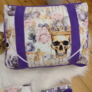 Coussin de lecture Vanité royale fait main avec un tissu côtelé violet et un tissu avec des motifs de tête de mort couronnée et des rose mauve et rose vue de haut