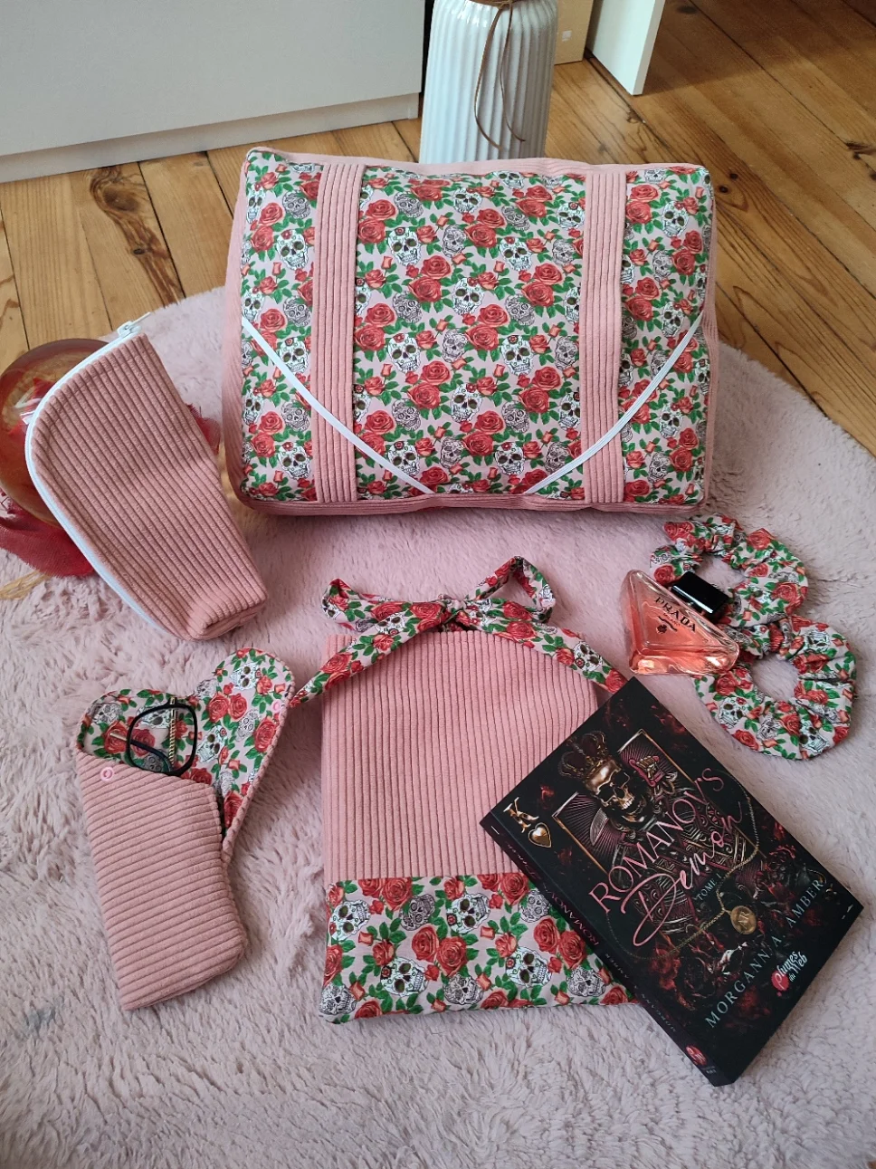 Ensemble de lecture Rose de l'ombre fait main avec un tissu Côtelé vieux rose et un tissu avec des motifs de cacatoès et de tête de mort et de rose rouge sur un fond rose vue de haut comprenant le coussin de lecture, le marque page, la pochette à livre, l'étui à lunette et la trousse