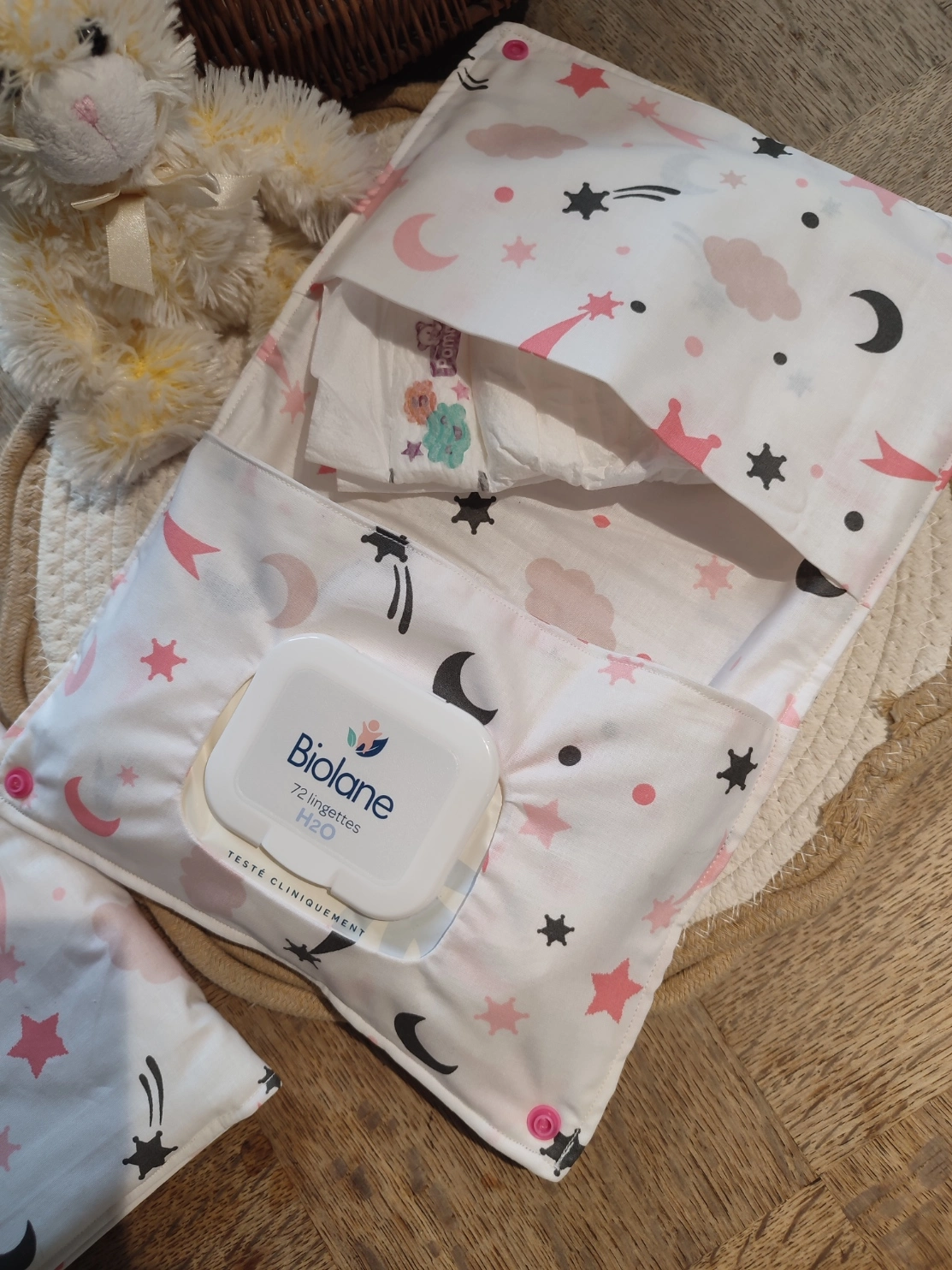 pochette à lange artisanale ouverte, elle est de couleur blanche avec des motifs d'étoile, de lune et de nuage de couleur rose et gris