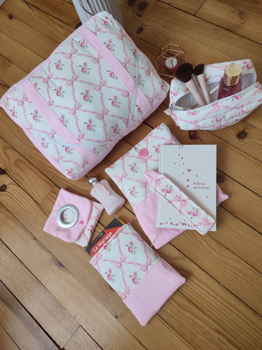 Ensemble de lecture ruban rose fait main avec un tissus représentant des noeuds rose et des rose fushia sur fond bland et un tissus côtelé rose. Comprenant le coussin de lecture, une pochette à livre grand et petit format, une trousse de toilette, un marque page et une pochette pour chargeur